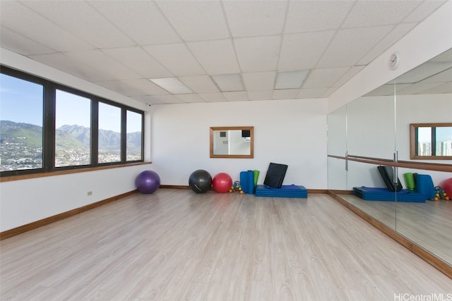 workout area featuring a mountain view, a drop ceiling, a healthy amount of sunlight, and light wood-type flooring