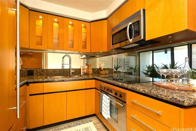 kitchen featuring sink, a textured ceiling, dark stone counters, stainless steel appliances, and light hardwood / wood-style floors