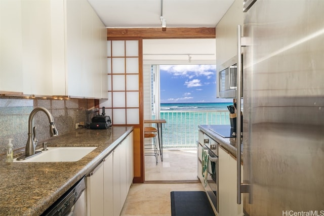 kitchen with appliances with stainless steel finishes, backsplash, sink, a water view, and white cabinetry