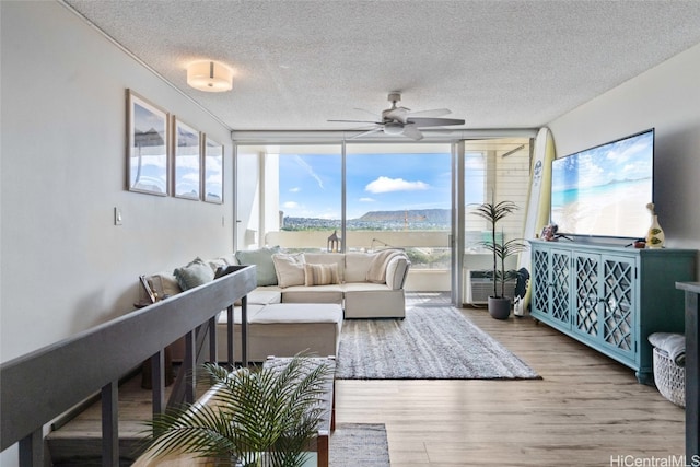 living room with ceiling fan, light hardwood / wood-style flooring, a textured ceiling, and a wall of windows