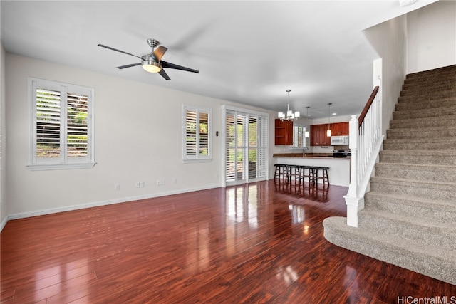 unfurnished living room featuring ceiling fan with notable chandelier, dark wood-type flooring, and a healthy amount of sunlight