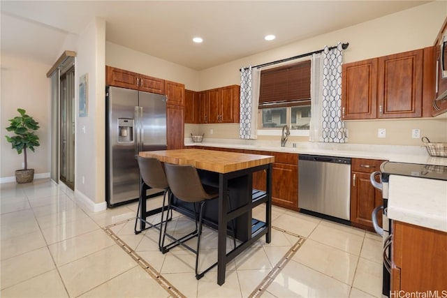 kitchen with wooden counters, a breakfast bar, stainless steel appliances, light tile patterned floors, and a center island