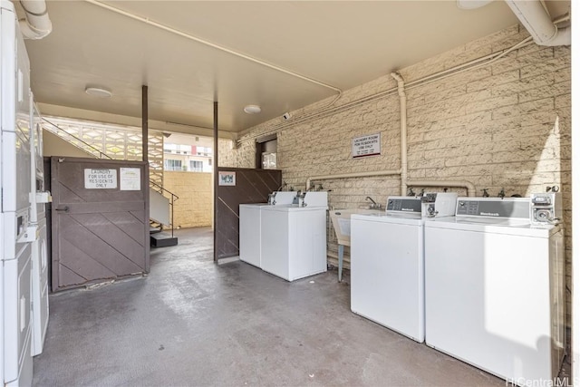 laundry area with brick wall, separate washer and dryer, and sink