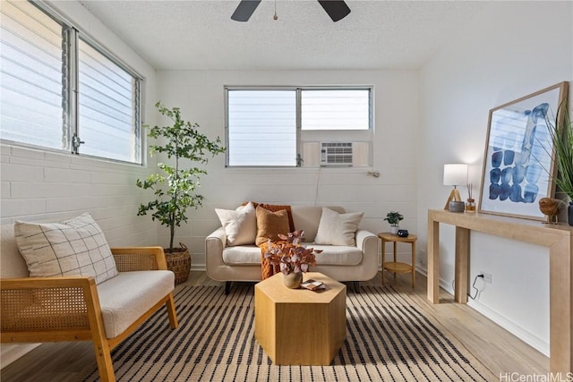 living area with ceiling fan, cooling unit, light hardwood / wood-style floors, and a textured ceiling