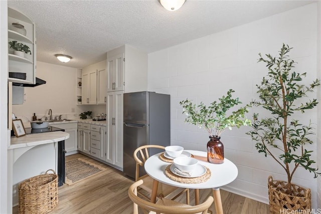 kitchen with light wood-type flooring, a textured ceiling, stainless steel refrigerator, and sink