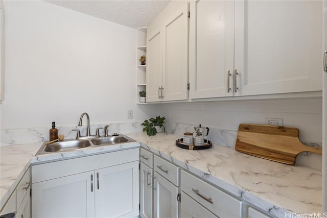 kitchen featuring white cabinetry, sink, light stone countertops, and a textured ceiling