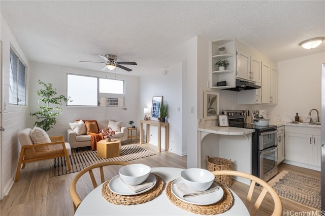 dining area featuring ceiling fan, sink, a textured ceiling, and light wood-type flooring