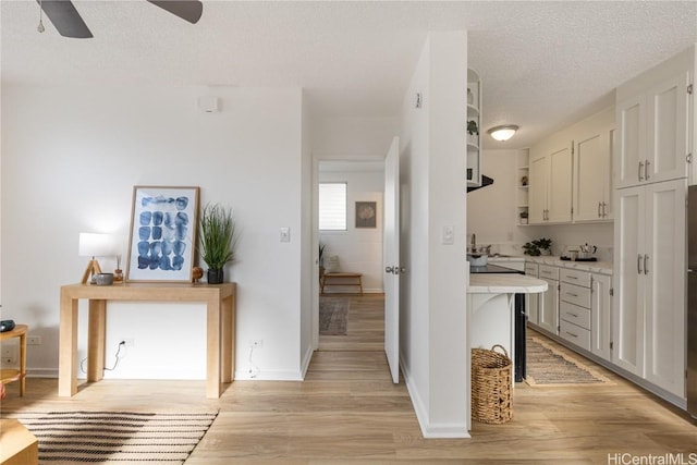 kitchen featuring ceiling fan, white cabinetry, a textured ceiling, and light hardwood / wood-style flooring