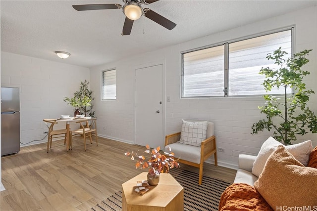 living room featuring ceiling fan, light hardwood / wood-style flooring, brick wall, and a textured ceiling