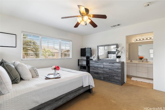 bedroom with light colored carpet, ensuite bath, and ceiling fan