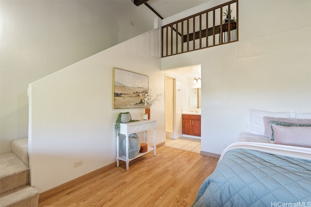 bedroom featuring ensuite bath, high vaulted ceiling, and light hardwood / wood-style flooring