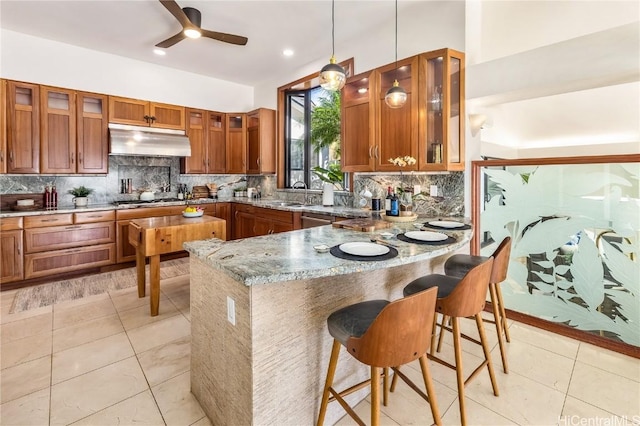 kitchen with kitchen peninsula, a kitchen breakfast bar, backsplash, stone countertops, and hanging light fixtures