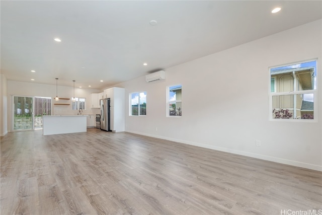 unfurnished living room featuring a wall mounted air conditioner, light hardwood / wood-style flooring, and sink