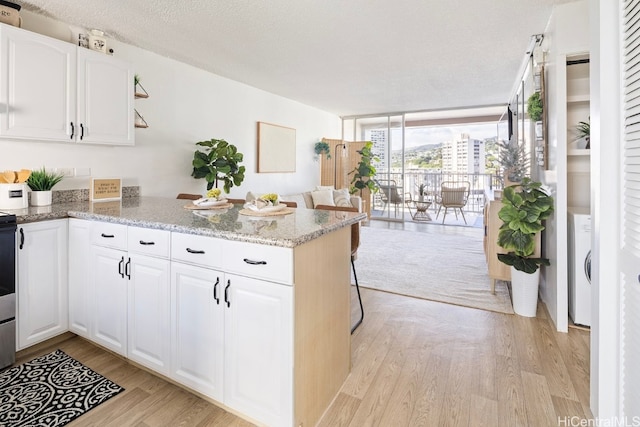 kitchen with kitchen peninsula, light wood-type flooring, white cabinetry, and light stone counters