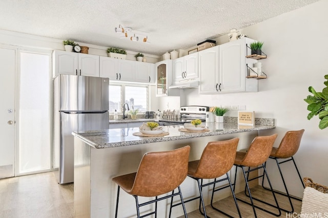 kitchen featuring kitchen peninsula, a textured ceiling, stainless steel appliances, white cabinetry, and a breakfast bar area