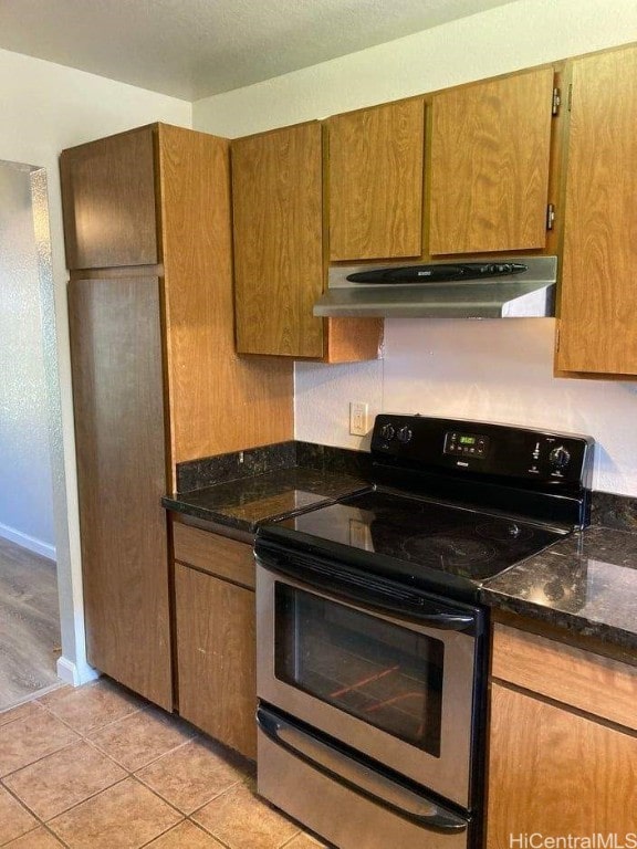 kitchen featuring dark stone countertops, light tile patterned flooring, and stainless steel electric range