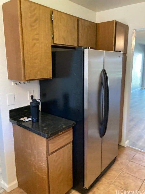 kitchen with stainless steel fridge, light tile patterned floors, and dark stone counters