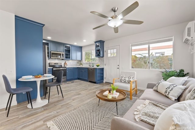 living room with light wood-type flooring, a wall unit AC, plenty of natural light, and ceiling fan