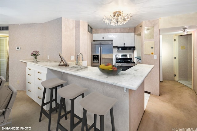 kitchen featuring white cabinets, a kitchen bar, kitchen peninsula, stainless steel appliances, and a chandelier