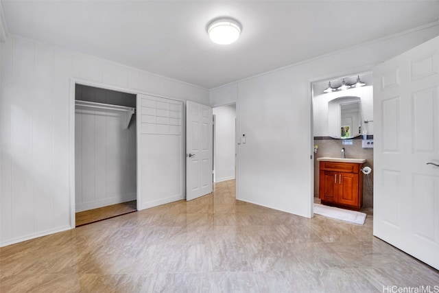 unfurnished bedroom featuring connected bathroom, a closet, crown molding, and sink