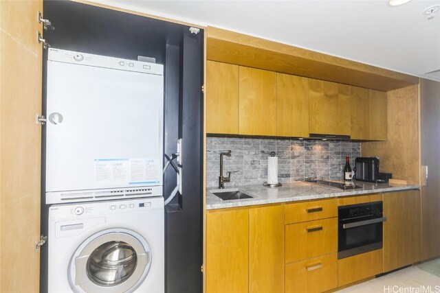 kitchen with stainless steel oven, black electric stovetop, sink, decorative backsplash, and stacked washing maching and dryer