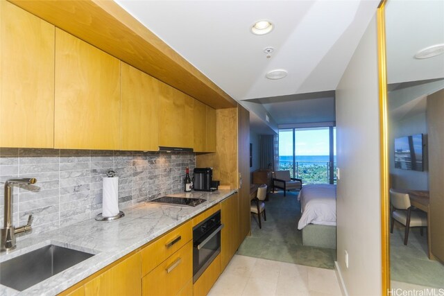 kitchen featuring decorative backsplash, black electric stovetop, light stone counters, stainless steel oven, and sink