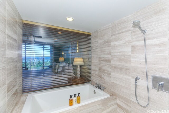 bathroom featuring a relaxing tiled tub and tile walls