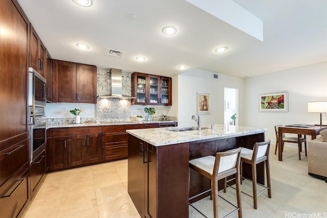 kitchen featuring backsplash, sink, wall chimney exhaust hood, an island with sink, and appliances with stainless steel finishes