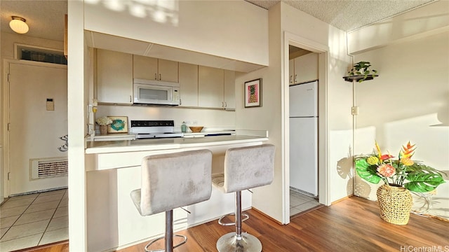 kitchen with a textured ceiling, light wood-type flooring, white appliances, and a breakfast bar area