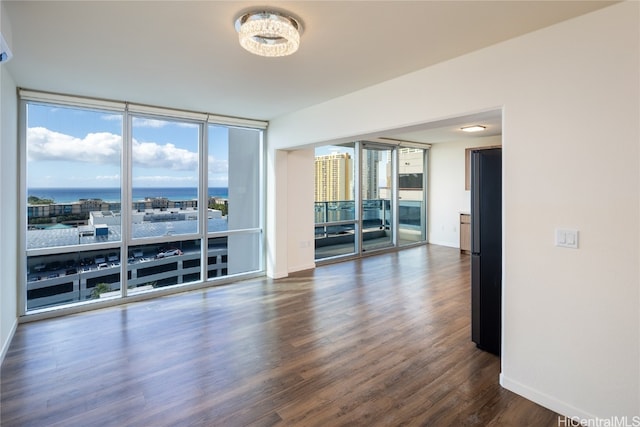 empty room featuring floor to ceiling windows, a water view, plenty of natural light, and dark wood-type flooring