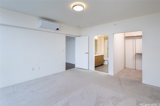 unfurnished bedroom with ensuite bath, a closet, light carpet, and a wall mounted AC