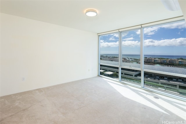 empty room featuring floor to ceiling windows, light colored carpet, and a water view