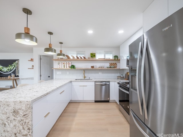 kitchen with backsplash, white cabinets, sink, hanging light fixtures, and appliances with stainless steel finishes