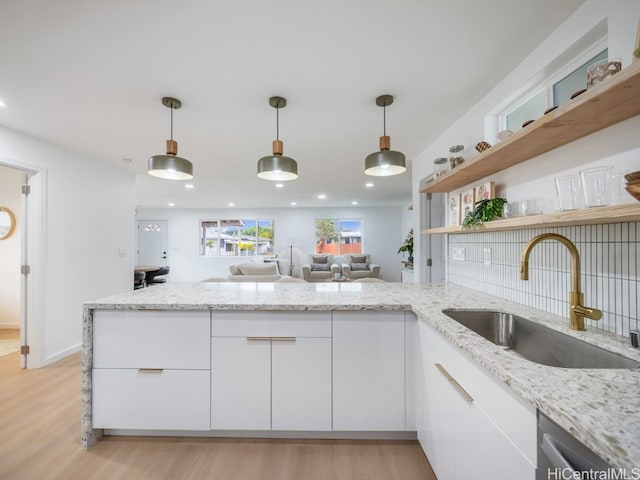 kitchen featuring light wood-type flooring, white cabinetry, sink, and hanging light fixtures