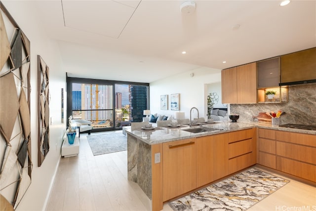 kitchen featuring kitchen peninsula, decorative backsplash, light stone countertops, sink, and light hardwood / wood-style floors