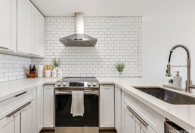 kitchen with a sink, white cabinetry, appliances with stainless steel finishes, backsplash, and wall chimney exhaust hood