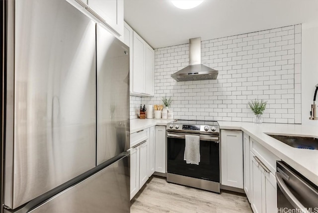 kitchen featuring white cabinets, wall chimney range hood, stainless steel appliances, and light countertops