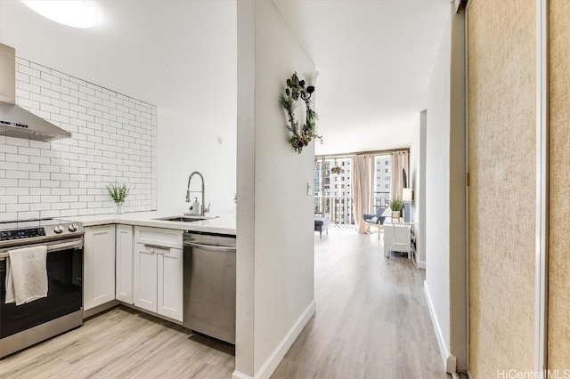 kitchen with appliances with stainless steel finishes, wall chimney exhaust hood, sink, light hardwood / wood-style flooring, and white cabinets