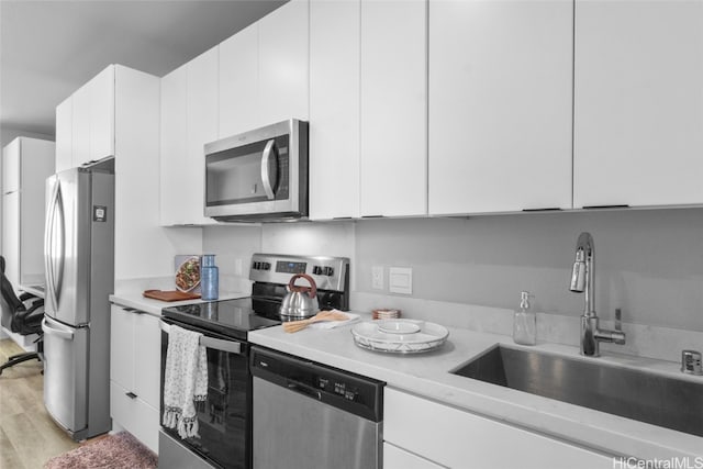 kitchen with white cabinets, appliances with stainless steel finishes, light hardwood / wood-style floors, and sink