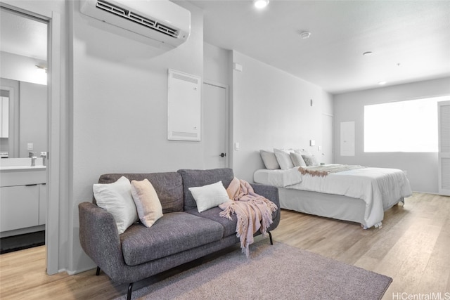 bedroom with a wall mounted air conditioner, light hardwood / wood-style flooring, and ensuite bath