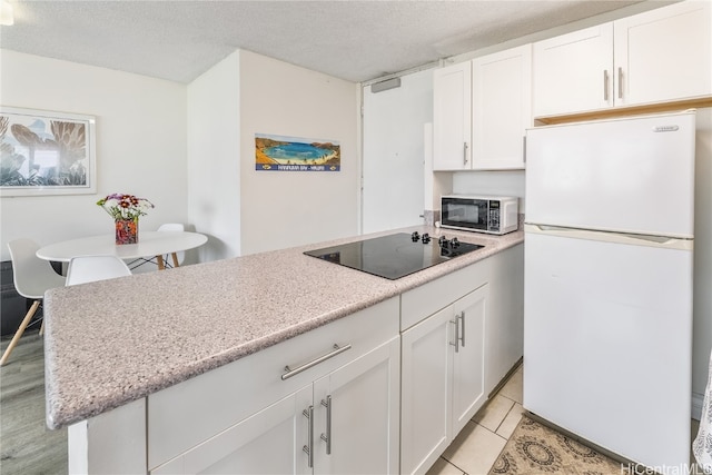 kitchen with white cabinets, black electric stovetop, white refrigerator, and a textured ceiling