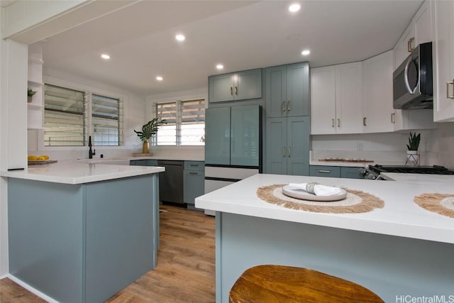 kitchen featuring a breakfast bar, sink, light hardwood / wood-style flooring, kitchen peninsula, and stainless steel appliances