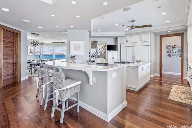 kitchen featuring white cabinetry, a large island, ceiling fan, dark hardwood / wood-style floors, and a kitchen bar