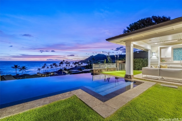 pool at dusk with a patio area, a yard, and a water view