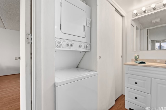 clothes washing area featuring a textured ceiling, dark hardwood / wood-style flooring, and stacked washer and clothes dryer