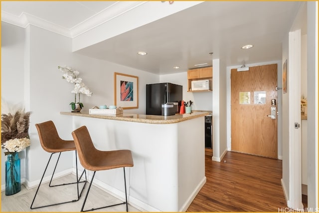 kitchen featuring black fridge, kitchen peninsula, crown molding, light hardwood / wood-style floors, and light brown cabinetry