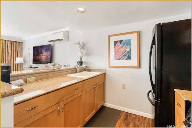 kitchen with dark wood-type flooring, black fridge, sink, a wall mounted AC, and light stone counters