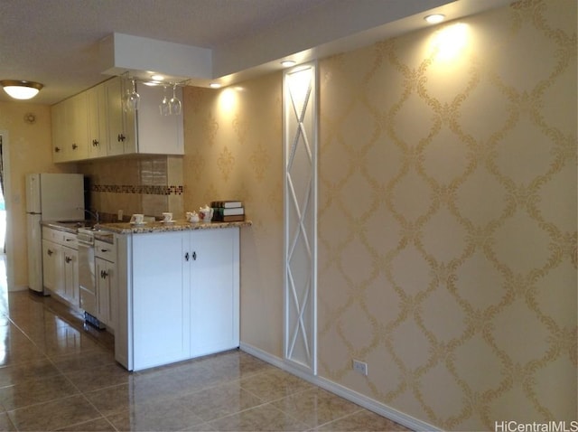 kitchen featuring white appliances, sink, tile patterned flooring, light stone countertops, and white cabinetry