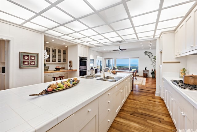 kitchen with white cabinets, tile countertops, light hardwood / wood-style floors, and sink