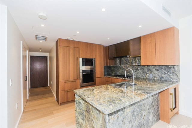 kitchen featuring sink, light hardwood / wood-style flooring, double oven, tasteful backsplash, and light stone counters